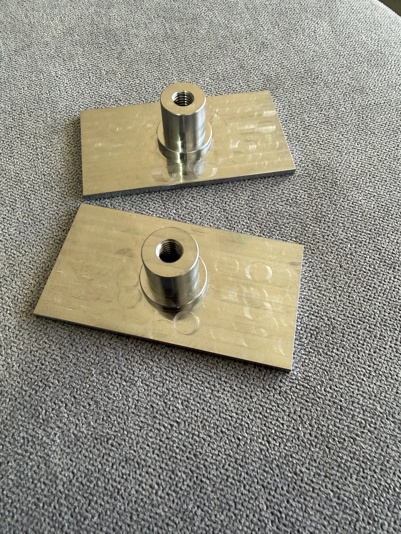 Two metal plates with cylindrical attachments on a textured surface.