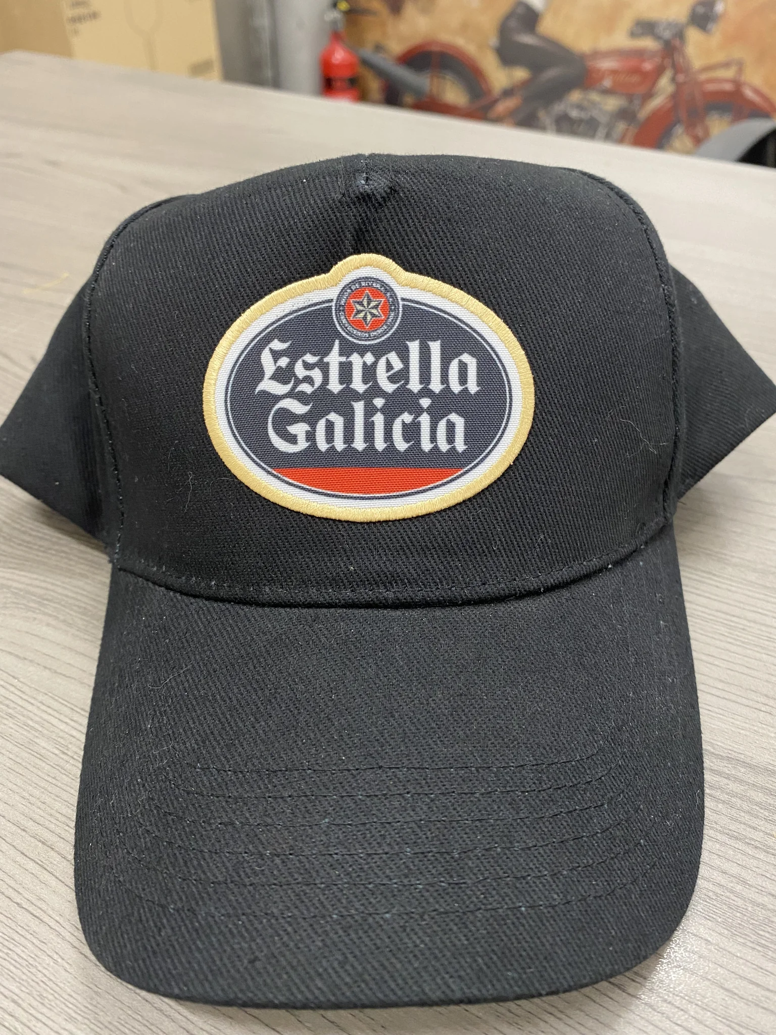 Black cap with Estrella Galicia embroidered logo, showcasing embroidery service.