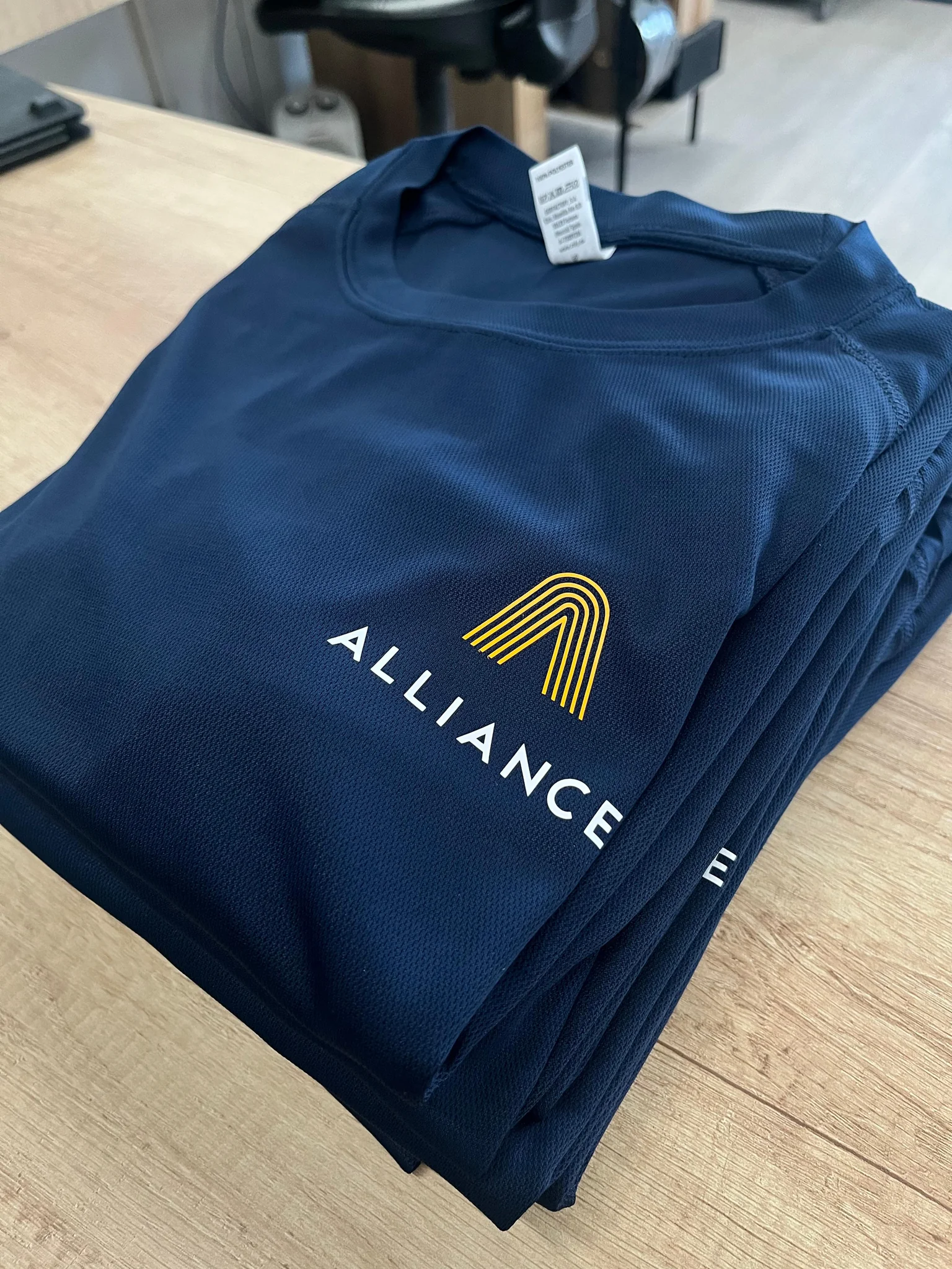 Stack of blue uniforms with embroidered logos for workwear embroidery service.