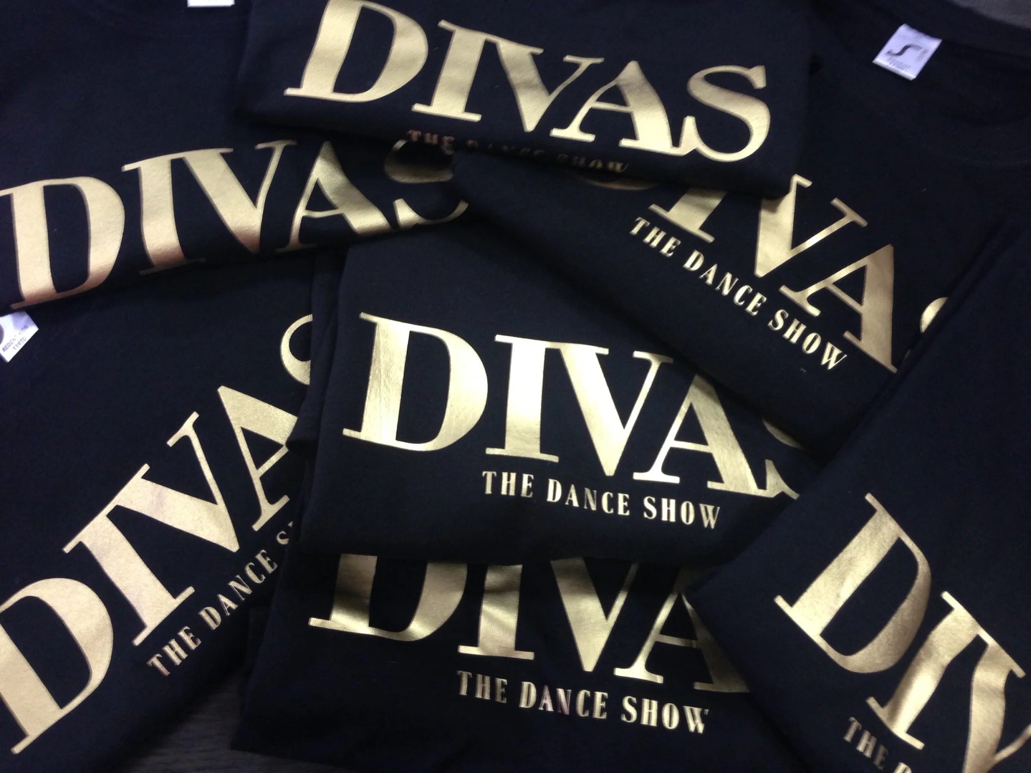 Printed t-shirts with 'DIVAS THE DANCE SHOW' in gold, showcasing t-shirt printing.