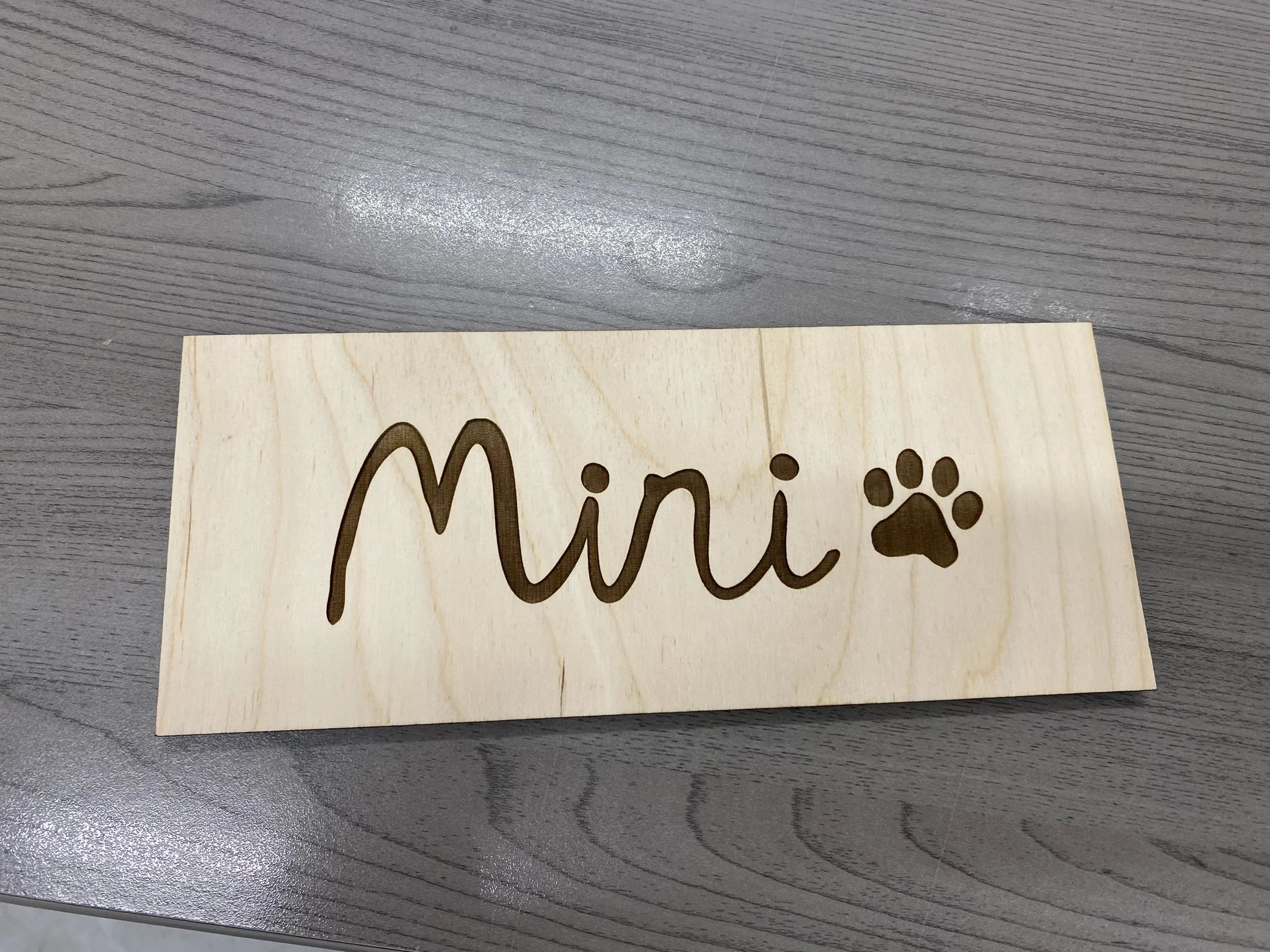 Engraved wooden plaque with 'Mini' and paw print, showcasing laser engraving.