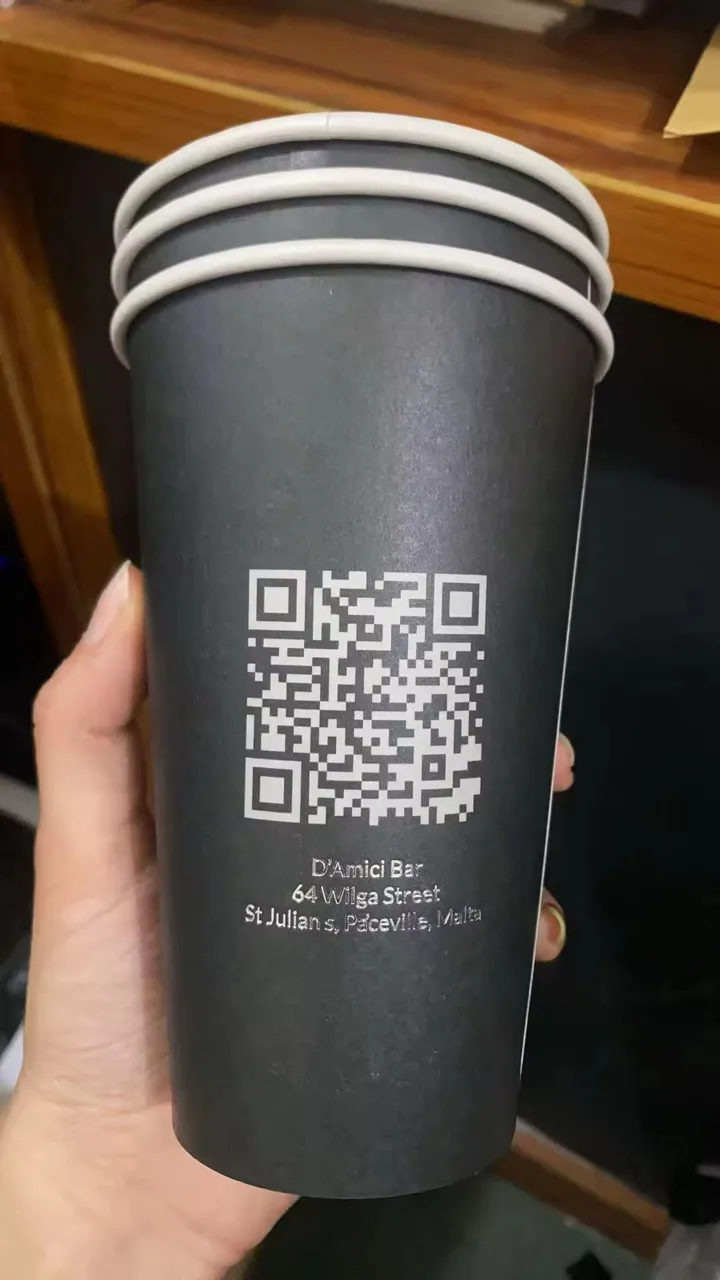 Black takeaway coffee cups printed with QR code and address for D'Amici Bar, St Julian's.
